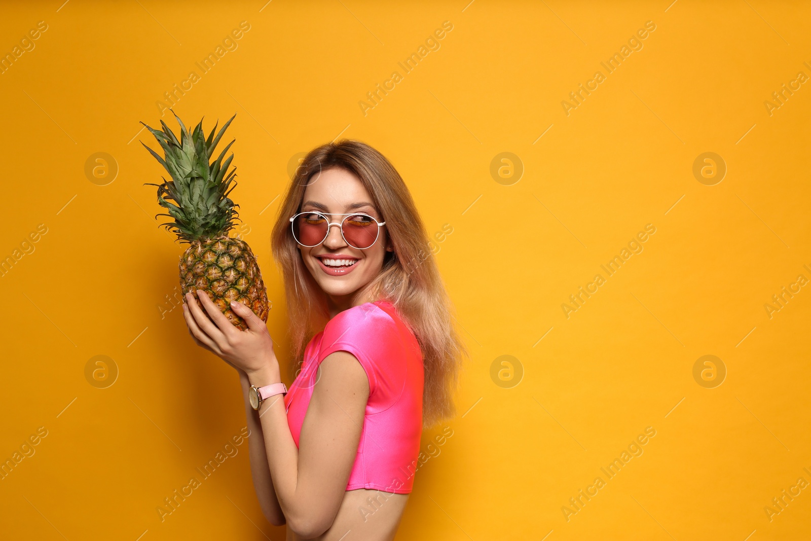 Photo of Young woman with fresh pineapple on yellow background, space for text. Exotic fruit