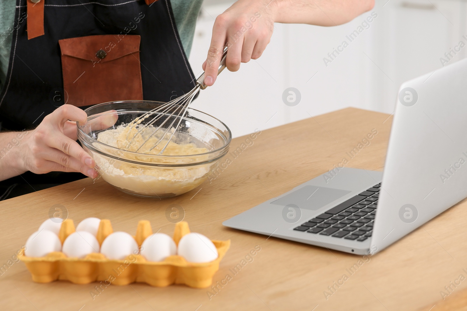 Photo of Man learning to cook with online video at wooden table indoors, closeup. Time for hobby