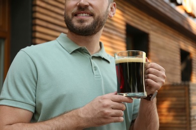 Photo of Young man with cold kvass outdoors, closeup. Traditional Russian summer drink