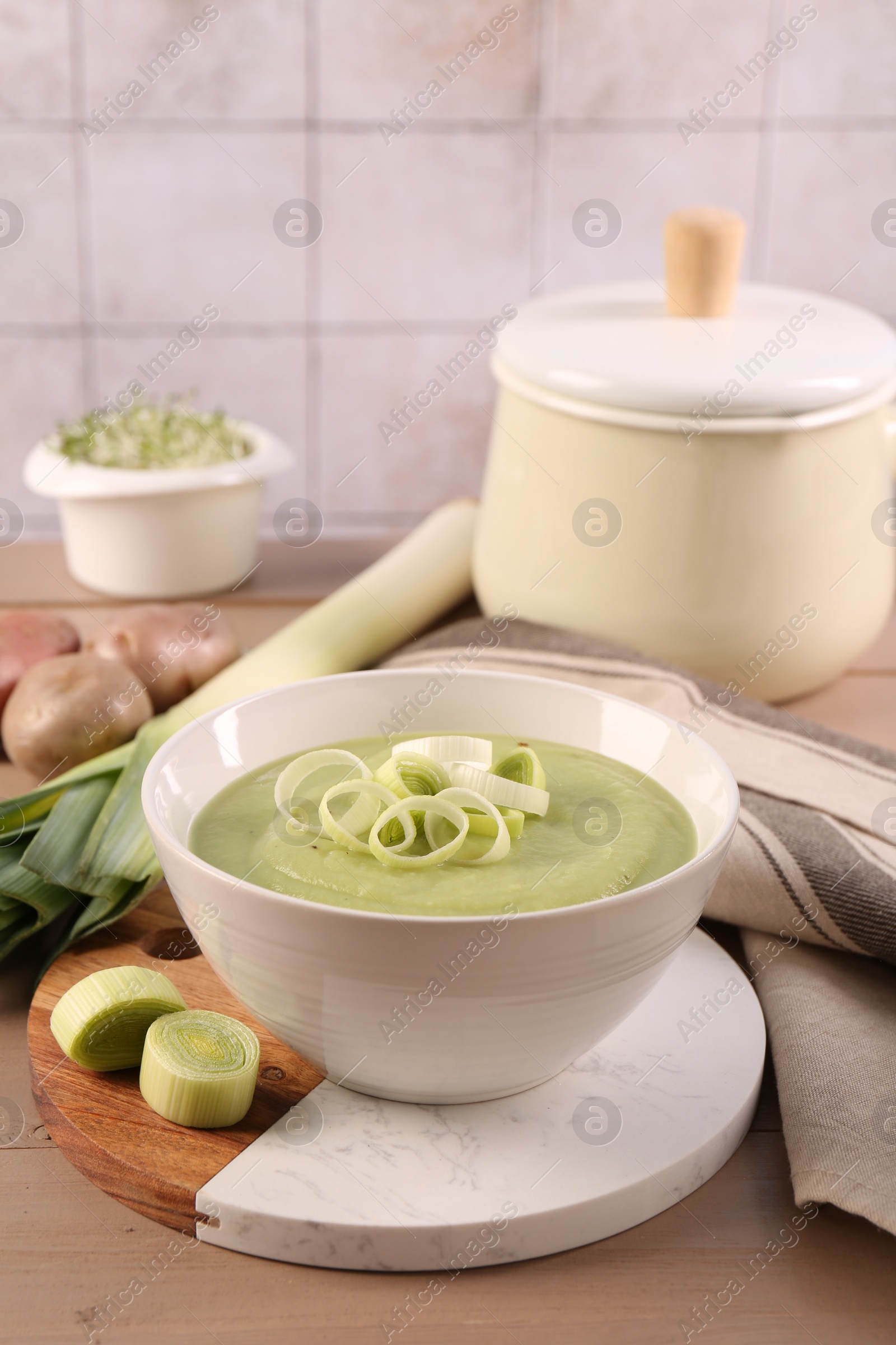 Photo of Tasty leek soup in bowl and fresh ingredients on wooden table