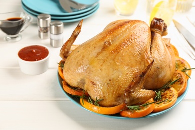 Photo of Delicious chicken with oranges and rosemary on white wooden table