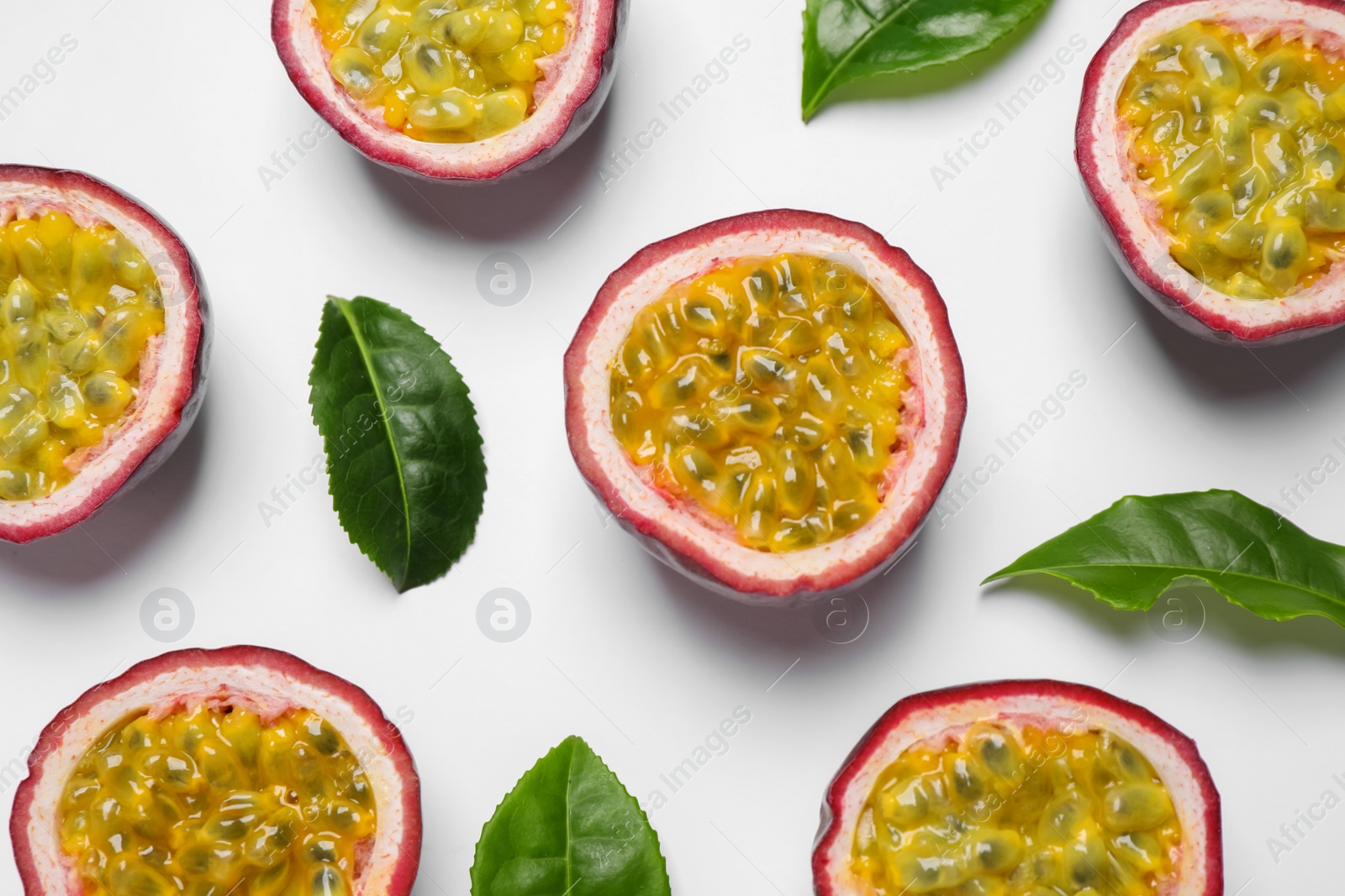 Photo of Halves of passion fruits (maracuyas) and green leaves on white background, flat lay