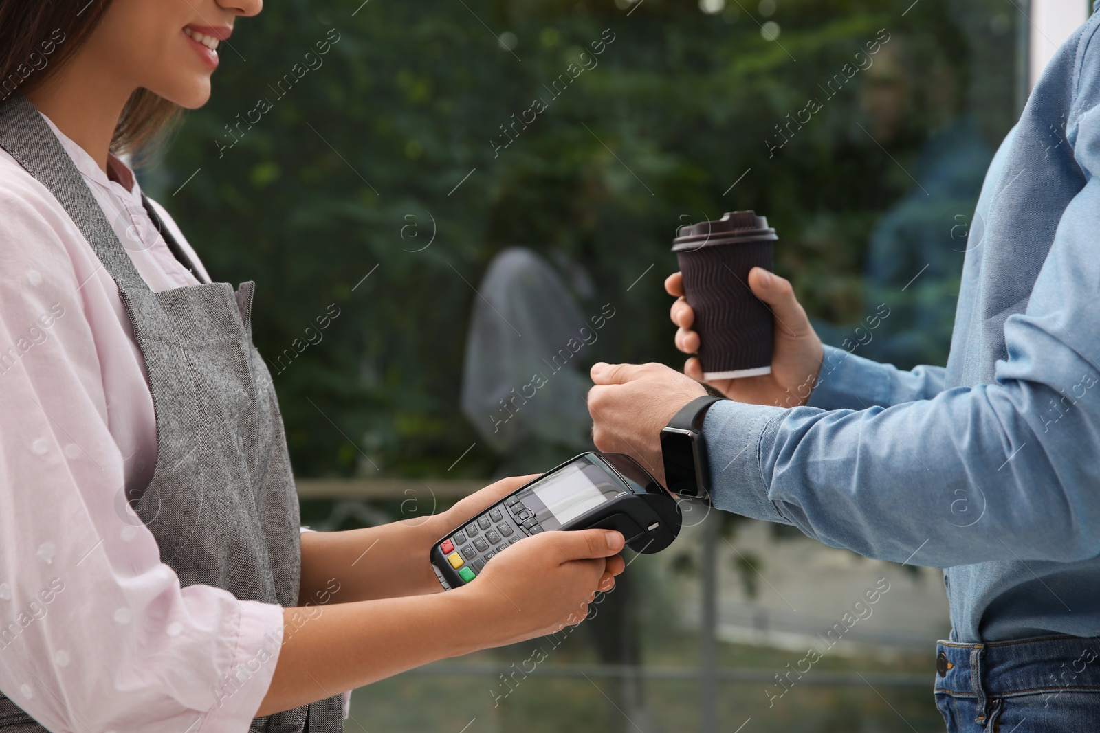 Photo of Man using smart watch for contactless payment via terminal in cafe, closeup