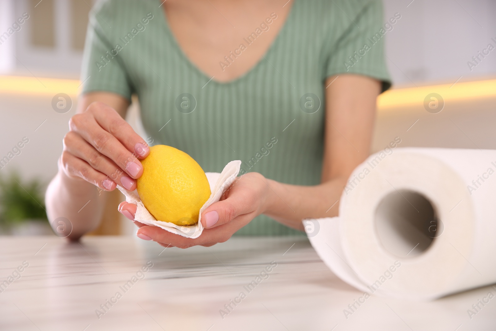 Photo of Woman wiping lemon with paper towel in kitchen, closeup