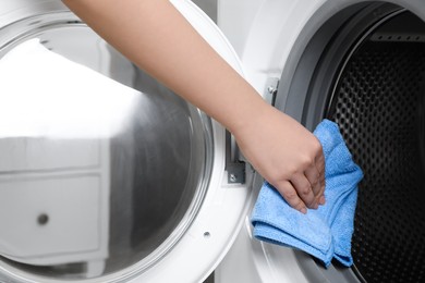 Photo of Woman cleaning empty washing machine with rag indoors, closeup