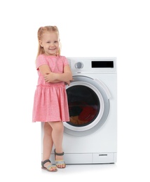 Cute little girl near washing machine with laundry on white background