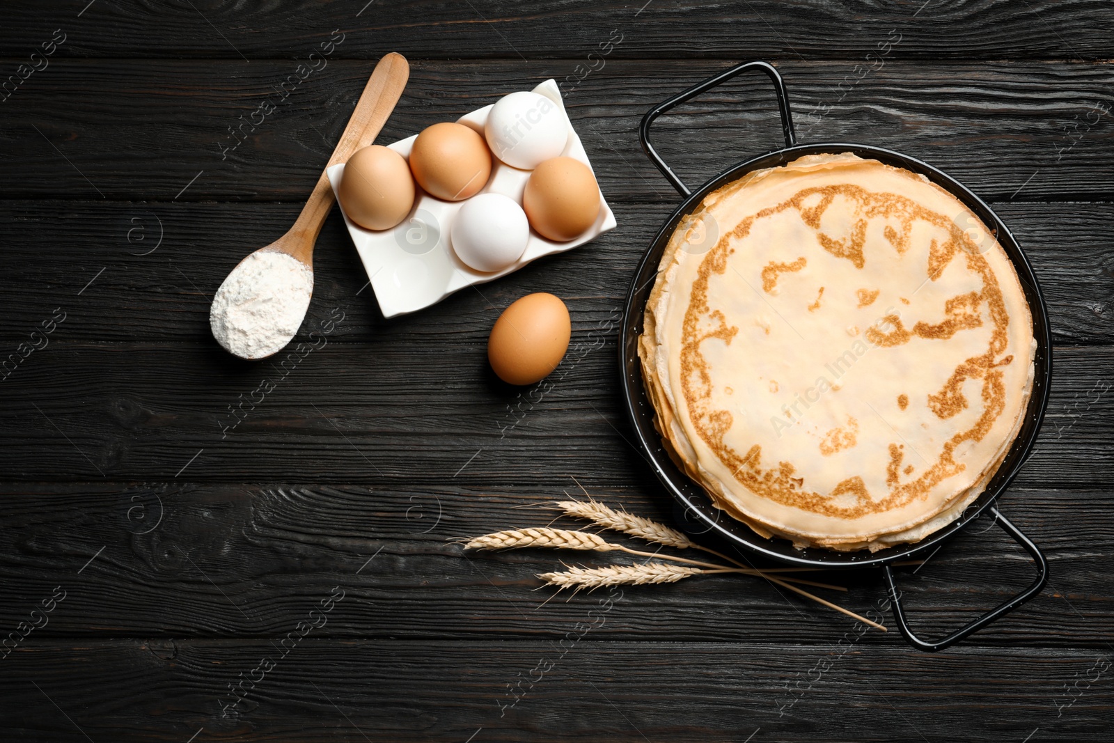 Photo of Dish with thin pancakes and ingredients on wooden background, top view