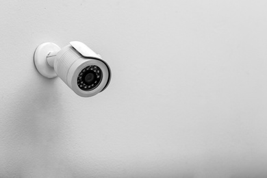 Photo of Modern CCTV security camera on white wall. Space for text