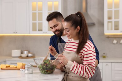 Photo of Happy affectionate couple cooking together at white table in kitchen