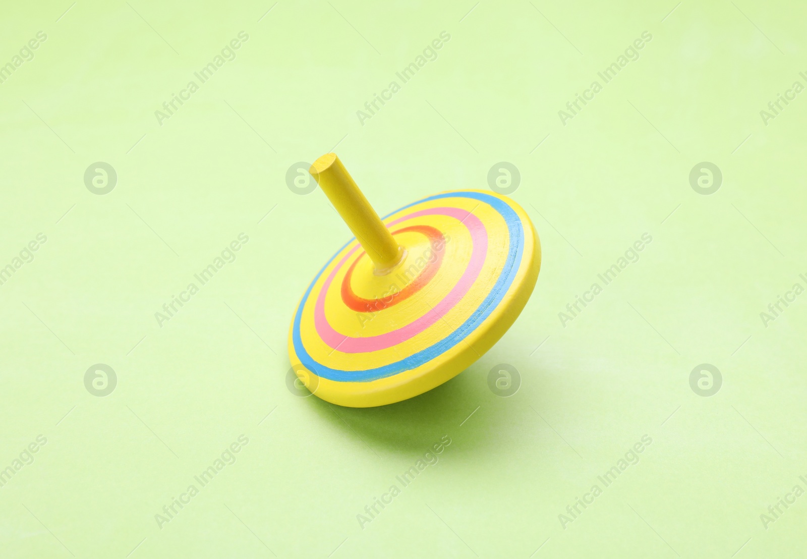 Photo of One bright spinning top on light green background. Toy whirligig