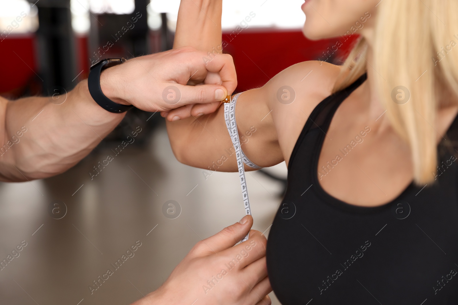 Photo of Trainer measuring woman`s biceps with tape in gym, closeup