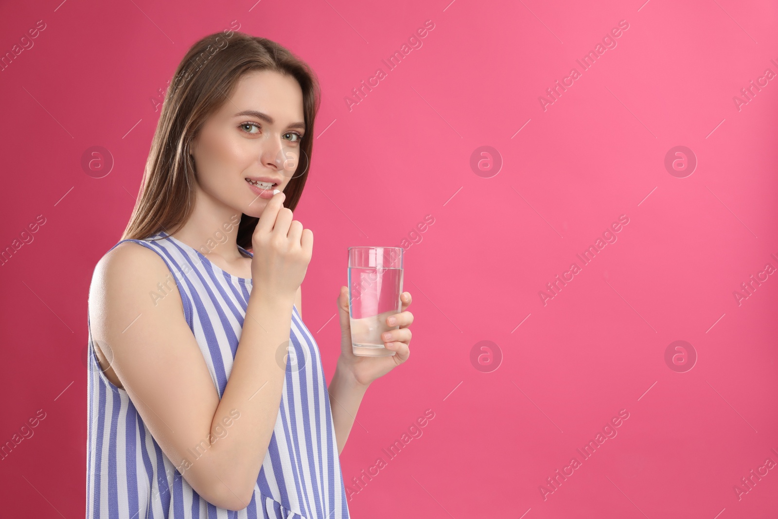 Photo of Young woman with glass of water taking vitamin pill on pink background. Space for text