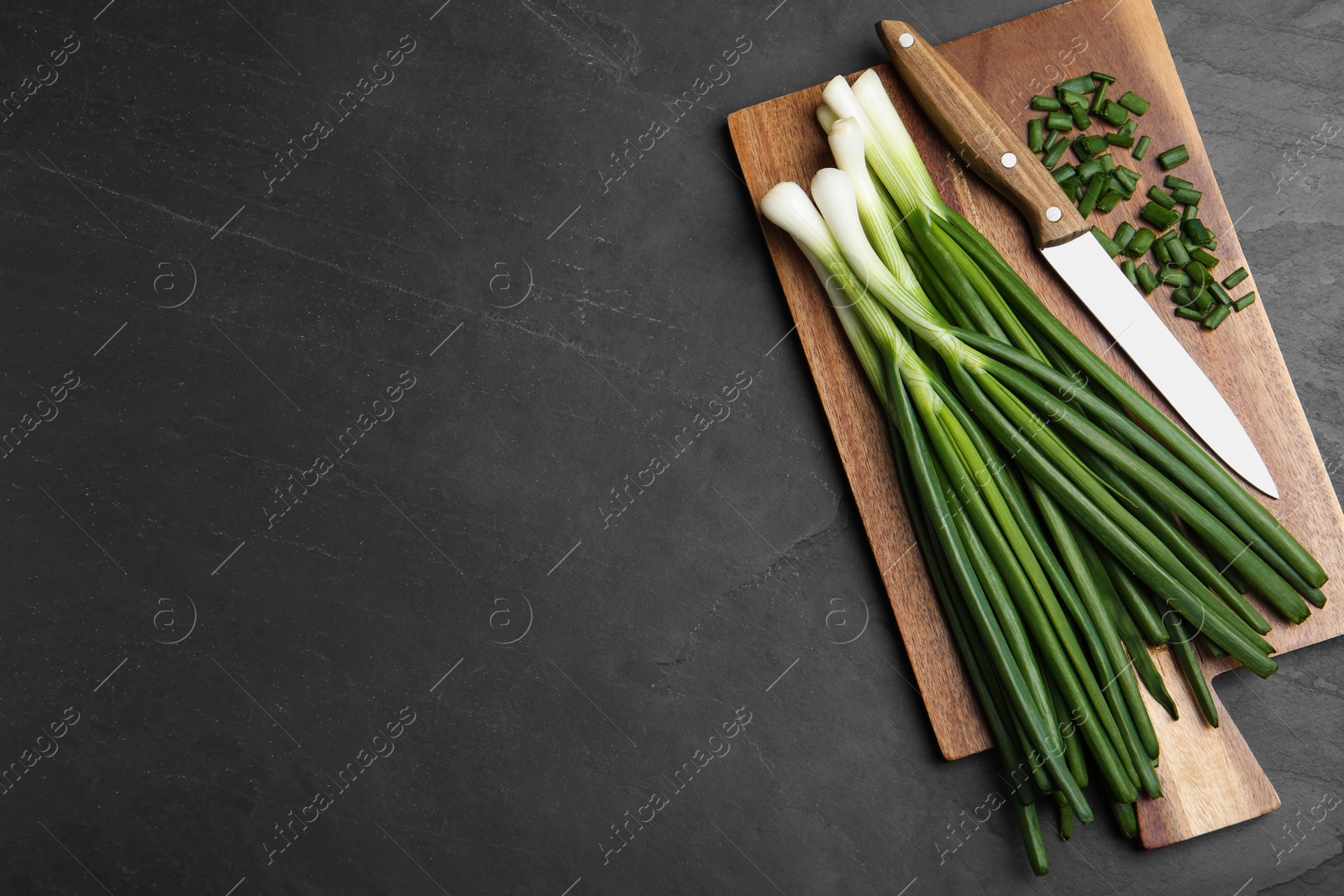 Photo of Fresh green spring onions, cutting board and knife on black table, top view. Space for text