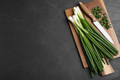 Photo of Fresh green spring onions, cutting board and knife on black table, top view. Space for text