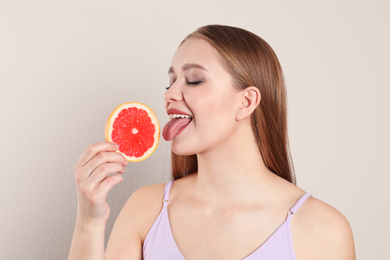 Photo of Young woman with cut grapefruit on beige background. Vitamin rich food