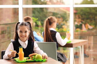 Photo of Happy girl at table with healthy food in school canteen