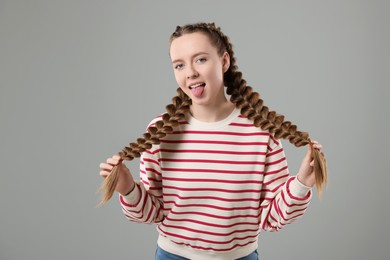 Photo of Woman with braided hair showing tongue on grey background