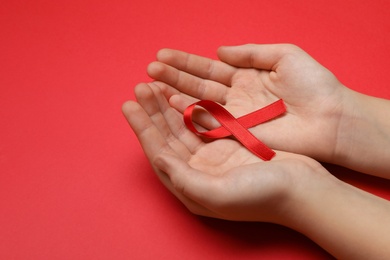 Photo of Little girl holding red ribbon on bright background, closeup. AIDS disease awareness