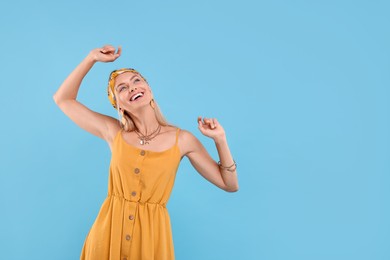 Photo of Portrait of smiling hippie woman dancing on light blue background. Space for text
