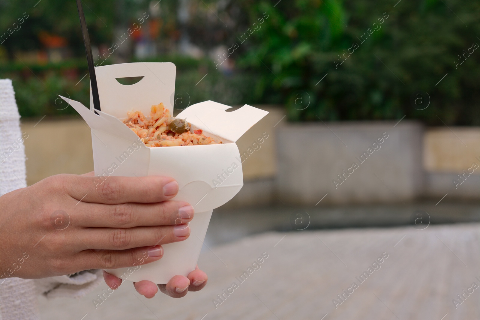 Photo of Woman holding paper box of takeaway noodles with fork outdoors, closeup and space for text. Street food