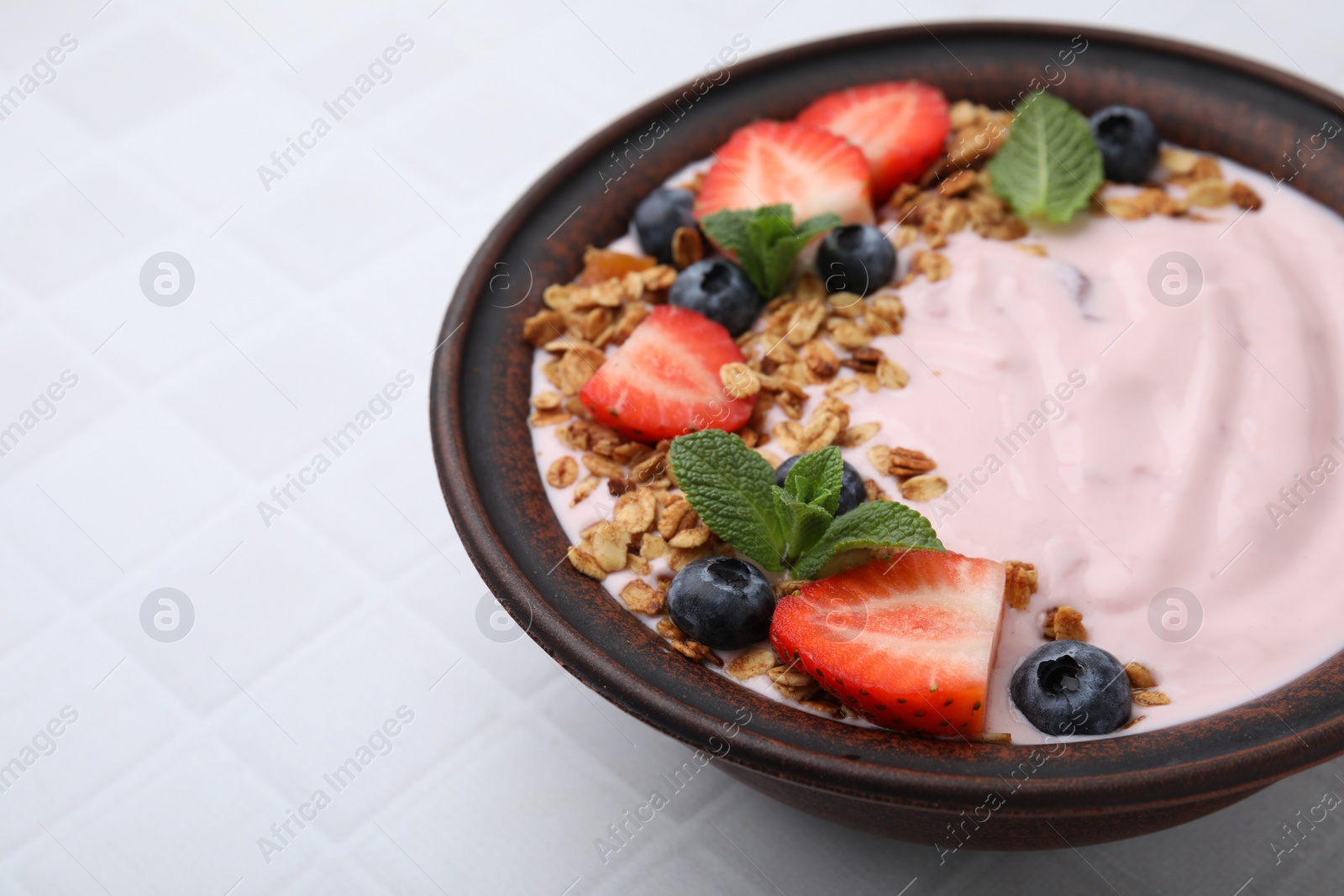 Photo of Bowl with yogurt, berries and granola on white tiled table, closeup. Space for text