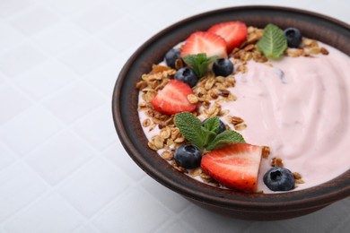 Photo of Bowl with yogurt, berries and granola on white tiled table, closeup. Space for text