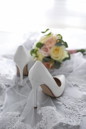 Photo of Pair of white high heel shoes, veil and wedding bouquet on light background