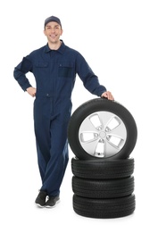 Young mechanic in uniform with car tires on white background