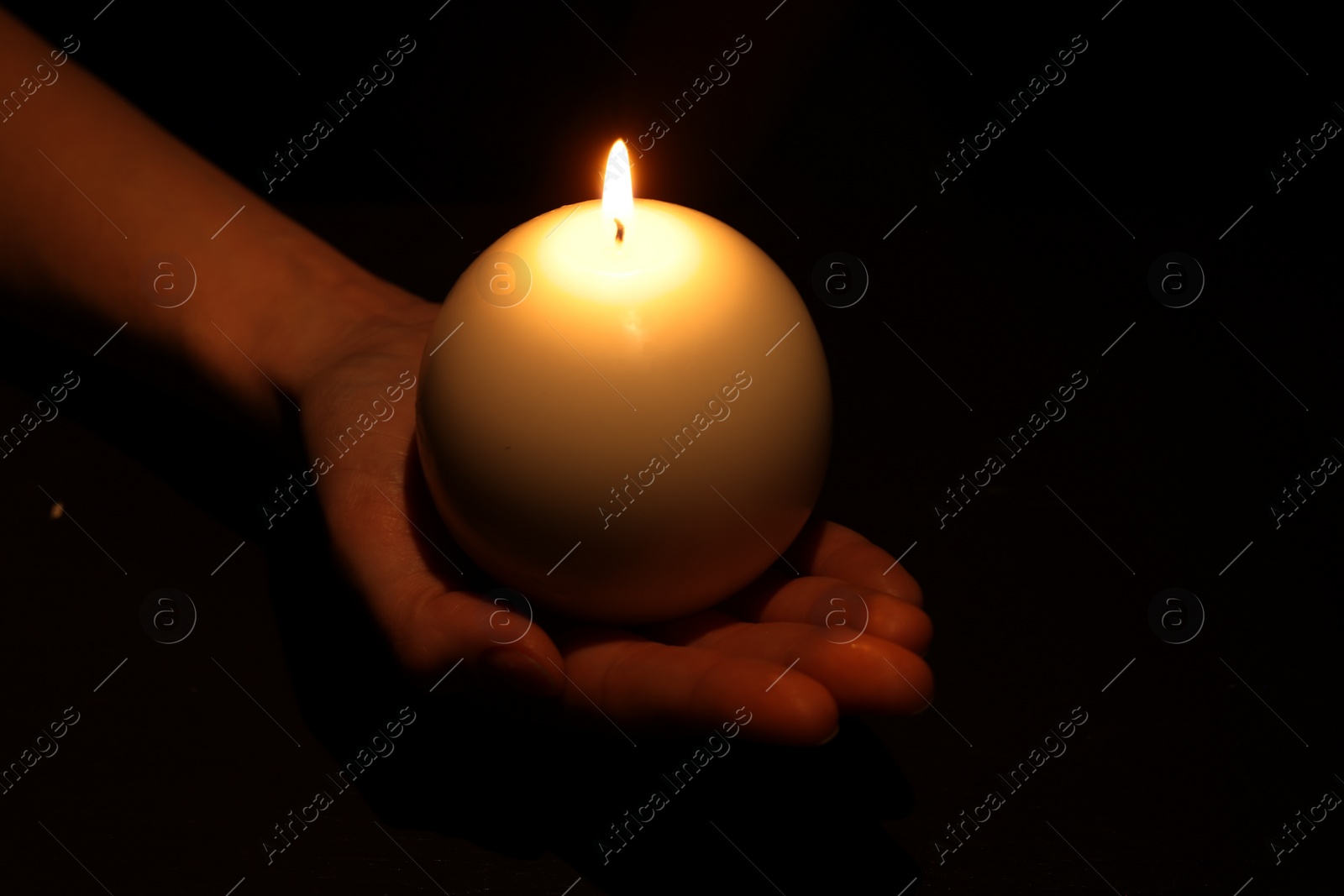Photo of Woman holding burning candle in hand on black background, closeup