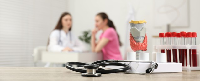 Endocrinologist examining patient at clinic, focus on stethoscope and model of thyroid gland. Banner design