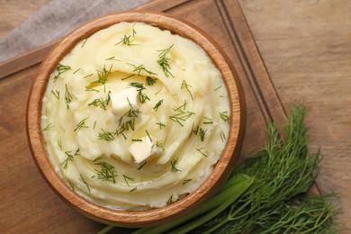 Photo of Bowl of delicious mashed potato with dill and butter on wooden table, flat lay