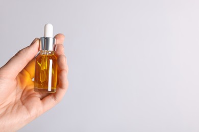 Photo of Woman holding bottle of cosmetic oil on light background, closeup. Space for text