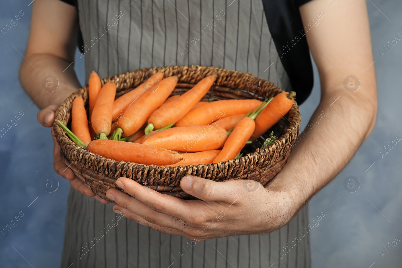 Photo of Young woman holding bowl with ripe carrots on color background, closeup