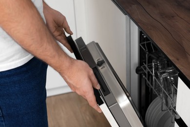 Man opening dishwasher's door in kitchen, closeup