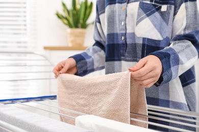 Young woman hanging clean laundry on drying rack at home, closeup