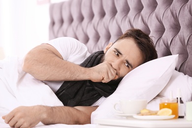 Photo of Ill man suffering from cough in bed at home