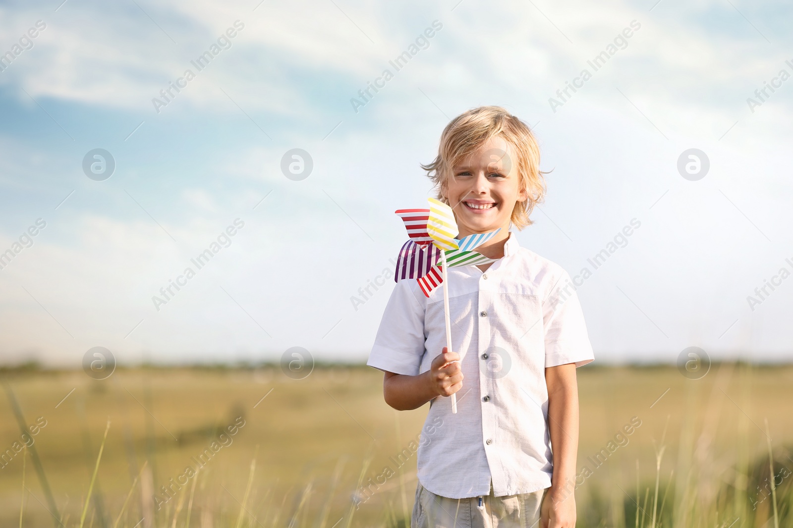 Photo of Cute little boy with pinwheel outdoors, space for text. Child spending time in nature