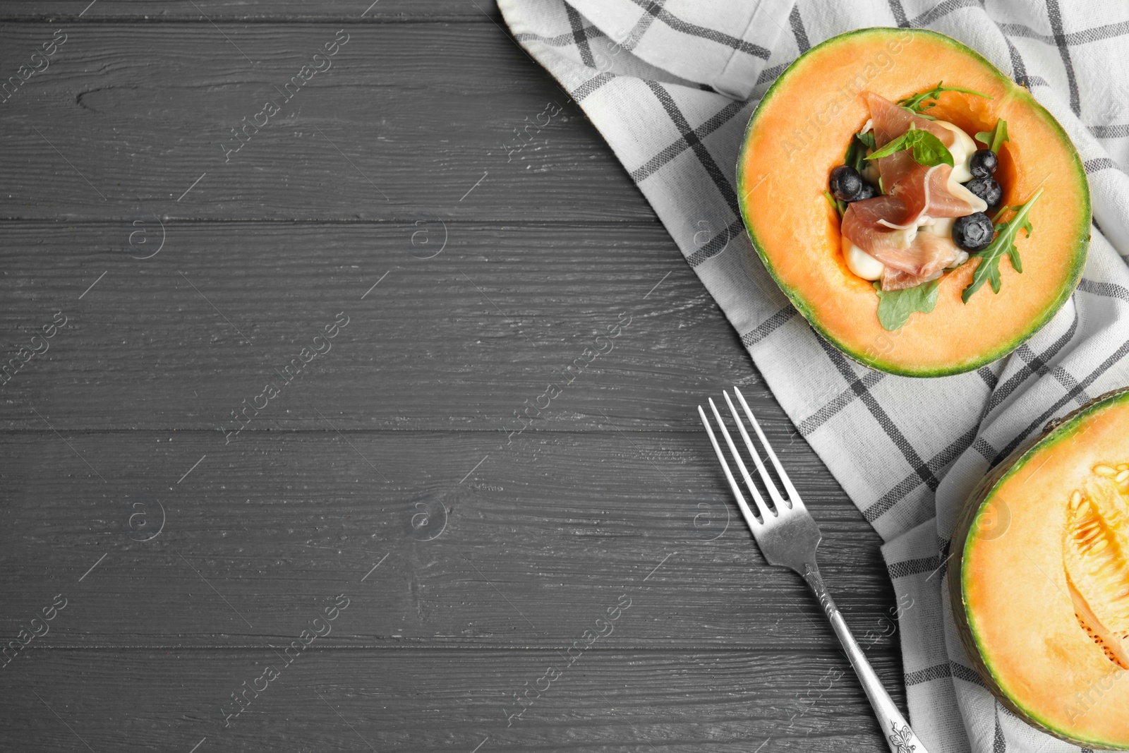 Photo of Flat lay composition of melon with prosciutto on grey wooden table. Space for text