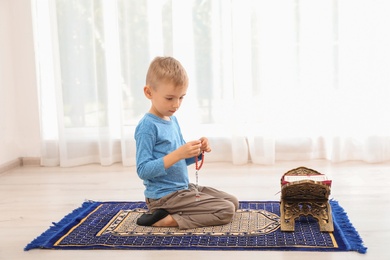 Photo of Little Muslim boy with misbaha and Koran praying on rug indoors