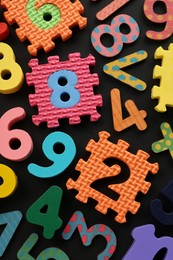 Photo of Many colorful numbers and mathematical symbols on black background, flat lay