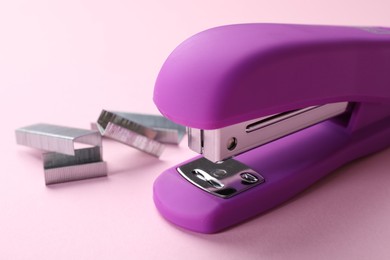 Bright stapler with staples on pink background, closeup