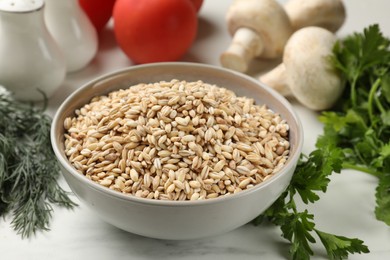 Photo of Dry pearl barley in bowl and products on white marble table