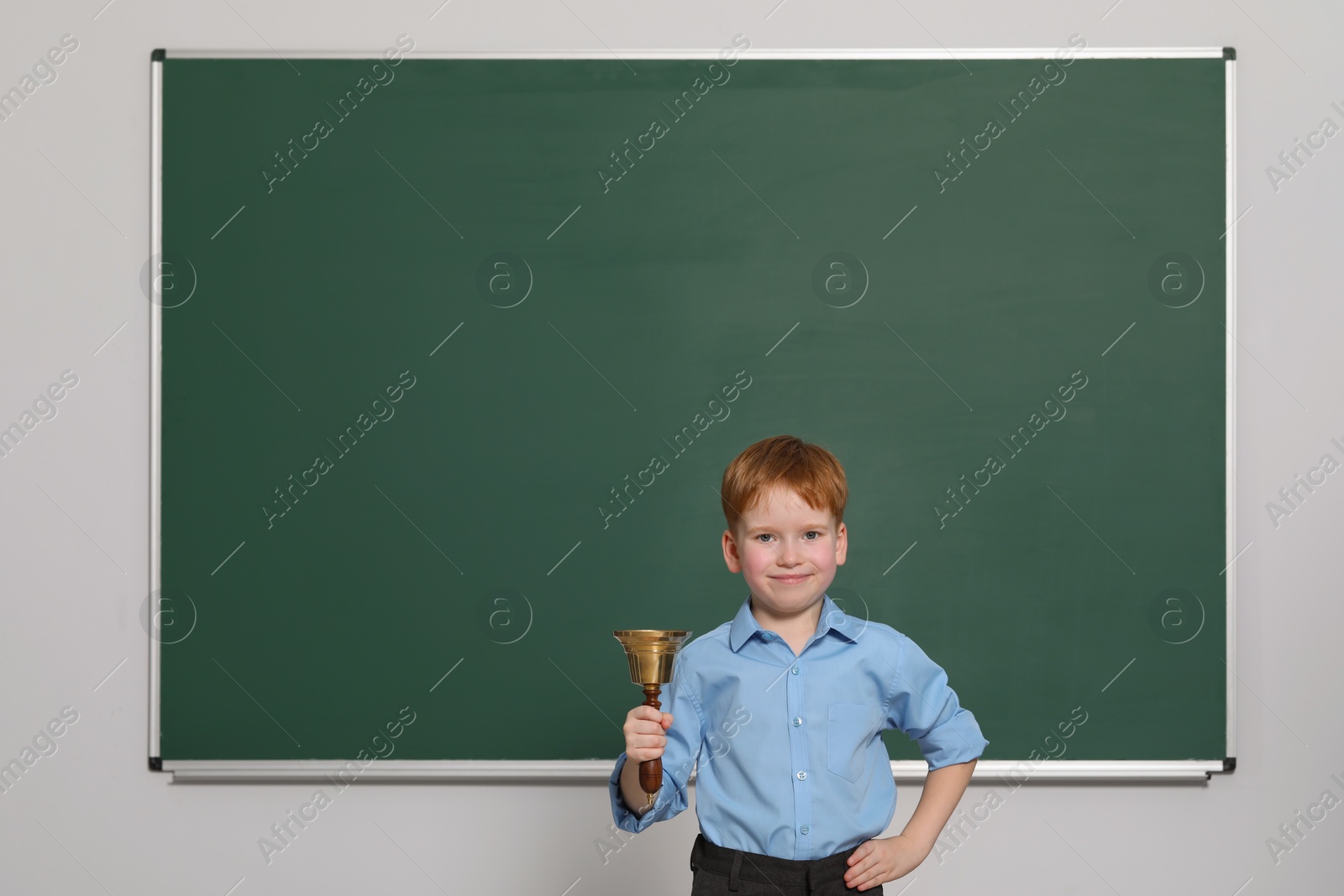 Photo of Pupil with school bell near green chalkboard in classroom