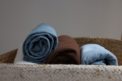 Photo of Different rolled shirts in basket against grey background, closeup. Organizing clothes