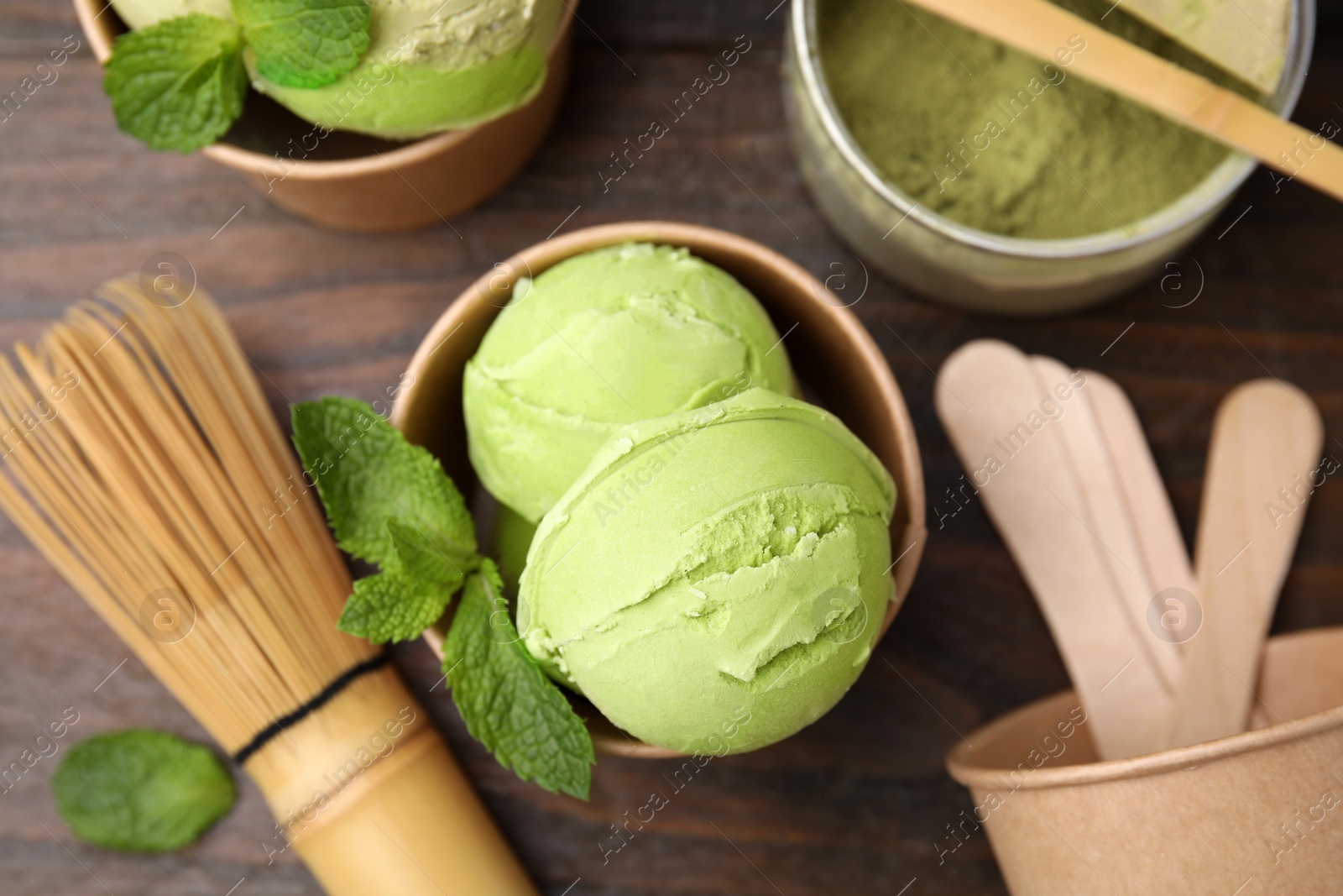 Photo of Paper cups with tasty matcha ice cream on wooden table, flat lay
