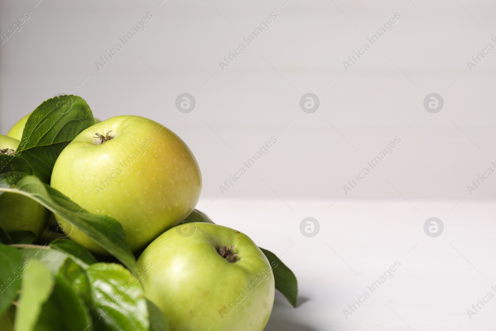 Photo of Fresh ripe green apples with leaves on white table, closeup. Space for text