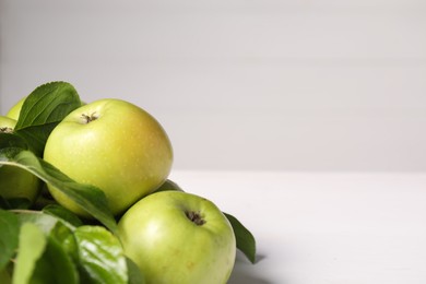 Fresh ripe green apples with leaves on white table, closeup. Space for text