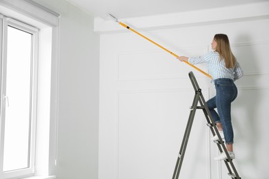 Photo of Young woman painting ceiling with white dye indoors, space for text