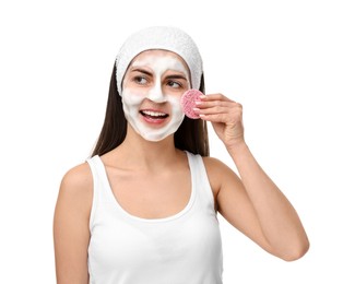 Young woman with headband washing her face using sponge on white background