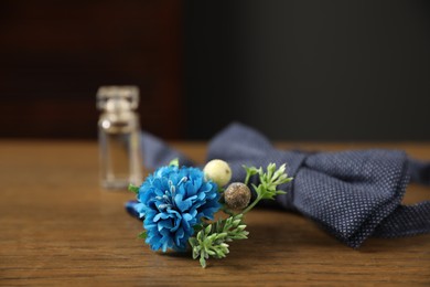 Photo of Wedding stuff. Stylish boutonniere, bow tie and perfume bottle on wooden table, closeup